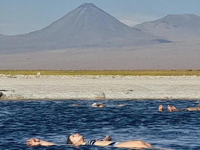 Des personnes flottent dans un lagon salé bleu foncé, avec un grand volcan en arrière-plan.