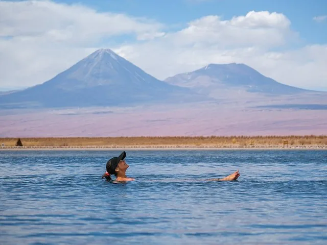 Une femme flotte paisiblement dans une lagune bleue avec de majestueuses montagnes en arrière-plan.