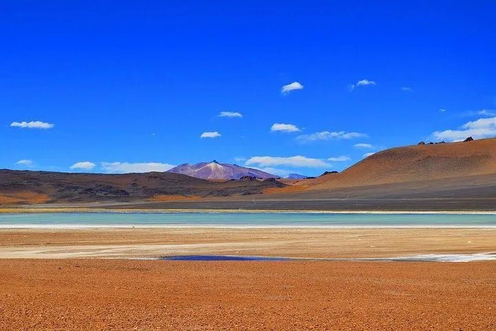 Une vue panoramique d’un lagon bleu-vert au milieu d’un paysage désertique sec et rouge.