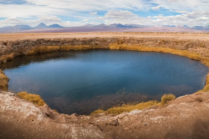 Une grande doline bleu foncé entourée d’herbes dorées et d’un vaste désert.