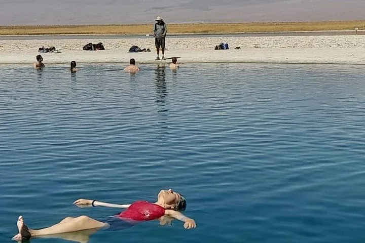 Eine Frau treibt in einer blauen Lagune, während andere sich am sandigen Ufer entspannen.