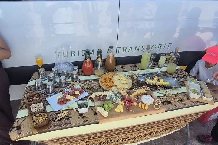 A table set with snacks, cheeses, meats, and drinks next to a tour van.