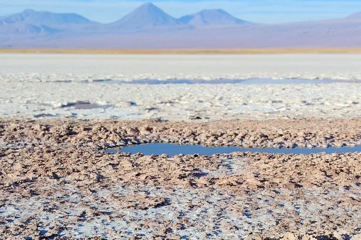 A small pool of water in a vast, dry salt flat with mountains beyond.
