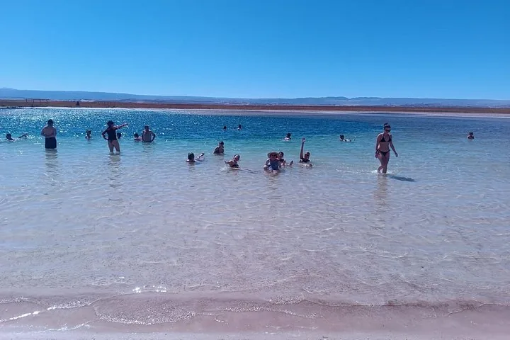 Several people wade and float in a clear, shallow lagoon on a sunny day.